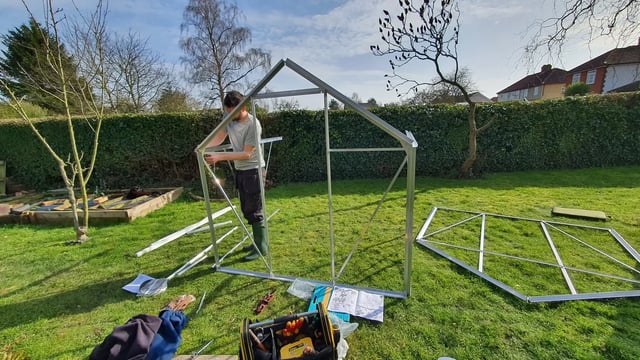 Volunteer building a greenhouse frame in a garden
